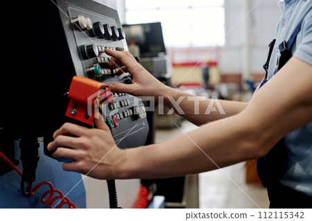 Unrecognizable young male specialist working in factory operating CNC machine Unrecognizable young male specialist working in factory operating CNC machine 112115342