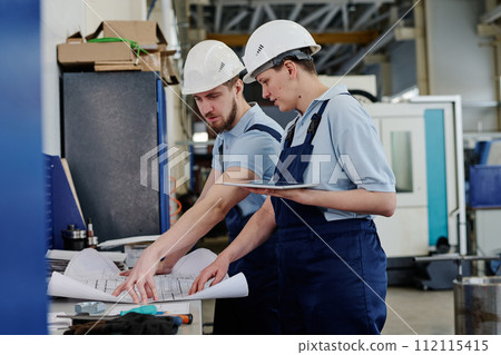 Professional drafter working in factory showing technical drawing to his female coworker, medium shot Professional drafter working in factory showing technical drawing to his female coworker, medium shot 112115415
