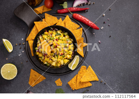 Freshly made mango salsa in a black ceramic bowl and nacho chips Freshly made mango salsa in a black ceramic bowl and nacho chips 112117564