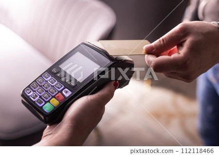 NFC credit card payment. Woman paying with contactless credit card with NFC technology. Wireless money transaction. Card machine in male hand on sunlight background 112118466