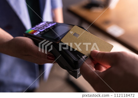 NFC credit card payment. Woman paying with contactless credit card with NFC technology. Wireless money transaction. Card machine in male hand on sunlight background NFC credit card payment. Woman paying with contactless credit card with NFC technology. Wireless money transaction. Card machine in male hand on sunlight background 112118472