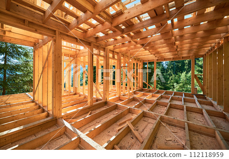 Under-construction residential wooden frame home located near a forest. Commencement of a new construction project for a cozy house or a mountain cottage. Idea of contemporary ecological construction. 112118959