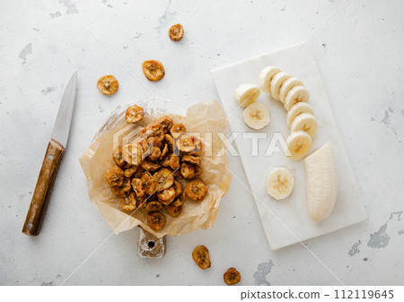 Dried round banana slices with fresh peeled banana and knife.Top view. 112119645