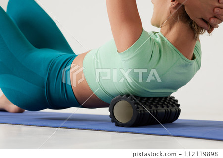 girl massages her back on a roller and does yoga on a white background, massage roller for fitness and yoga, Home training 112119898