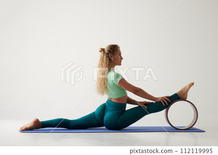 young flexible girl doing gymnastics, flexibility and stretching using a yoga wheel online on a white background 112119995
