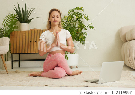 young flexible girl doing yoga, gymnastics, flexibility and stretching online at home in a bright room 112119997