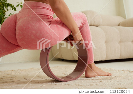 young flexible girl doing gymnastics, flexibility and stretching using a yoga wheel online on a white background 112120034
