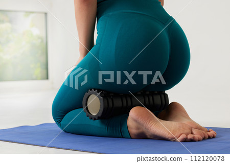 girl massages her legs on a roller and does yoga on a white background, massage roller for fitness and yoga, Home training girl massages her legs on a roller and does yoga on a white background, massage roller for fitness and yoga, Home training 112120078