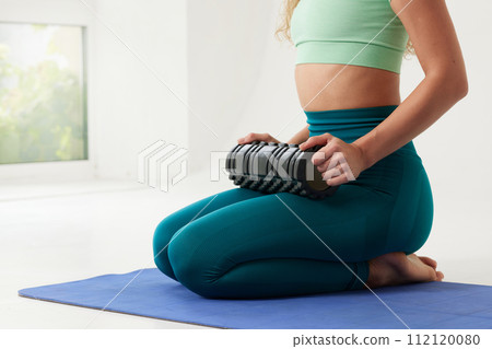 girl massages her back on a roller and does yoga on a white background, massage roller for fitness and yoga, Home training girl massages her back on a roller and does yoga on a white background, massage roller for fitness and yoga, Home training 112120080