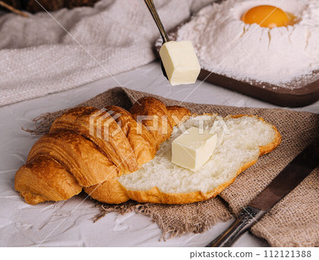 hands cut a fresh croissant and spreading butter hands cut a fresh croissant and spreading butter 112121388