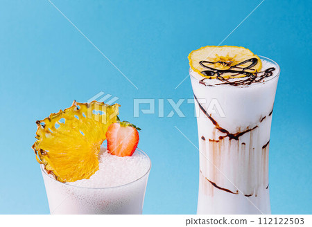 two glass cups of milkshake with dry pineapple and strawberries 112122503