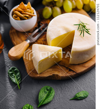 Round cheese on a wooden board and green grapes Round cheese on a wooden board and green grapes 112124701