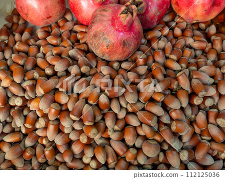 Lots of hazelnuts and pomegranate fruits. Background from unpeeled walnut. Hazelnut pattern. Market stall. Selection of ingredients in the market. Healthy food. 112125036