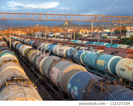 Tanks with fuel on the railway tracks at sunset. Sunset at the train station. The cargo part of the station. industrial zone against the backdrop of mountains. Fuel wagons. Cargo transportation Tanks with fuel on the railway tracks at sunset. Sunset at the train station. The cargo part of the station. industrial zone against the backdrop of mountains. Fuel wagons. Cargo transportation 112125184