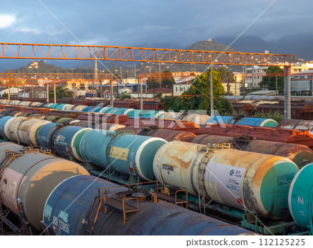 Tanks with fuel on the railway tracks at sunset. Sunset at the train station. The cargo part of the station. industrial zone against the backdrop of mountains. Fuel wagons. Cargo transportation Tanks with fuel on the railway tracks at sunset. Sunset at the train station. The cargo part of the station. industrial zone against the backdrop of mountains. Fuel wagons. Cargo transportation 112125225
