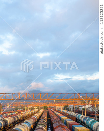 Tanks with fuel on the railway tracks at sunset. Sunset at the train station. The cargo part of the station. industrial zone against the backdrop of mountains. Fuel wagons. Cargo transportation Tanks with fuel on the railway tracks at sunset. Sunset at the train station. The cargo part of the station. industrial zone against the backdrop of mountains. Fuel wagons. Cargo transportation 112125231