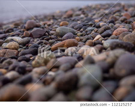 Pebbles on the seashore close-up. Rocky beach. Stones close-up with bokeh. Gray natural background. The concept of rest on the seashore. The Velvet season.  Waves and wet pebbles 112125257