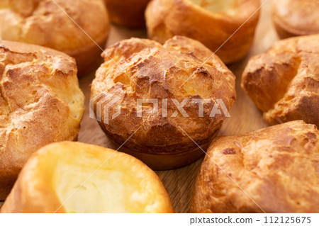 A lot of fresh hot popovers on wood plate or wooden board. Easy cooking, tasty breakfast, close up. Yorkshire pudding A lot of fresh hot popovers on wood plate or wooden board. Easy cooking, tasty breakfast, close up. Yorkshire pudding 112125675
