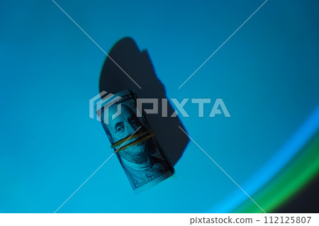 One hundred dollar bills rolled up under hard blue light 112125807