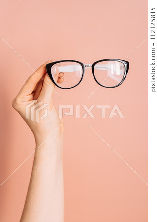 Vision glasses with black frames in a woman's hand against a pink background Vision glasses with black frames in a woman's hand against a pink background 112125815