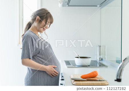 Pregnant woman smiling looking at her growing belly in the kitchen 112127282