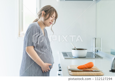 Pregnant woman who feels stomach pain while cooking in the kitchen (labour pain, water rupture, threatened premature birth) Pregnant woman who feels stomach pain while cooking in the kitchen (labour pain, water rupture, threatened premature birth) 112127294