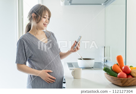 Pregnant women, maternity mothers, and pre-moms using smartphones in the kitchen at home 112127304