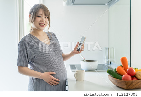 Pregnant woman using smartphone in the kitchen (maternity/app/nutrition management/meal management/meal record) 112127305