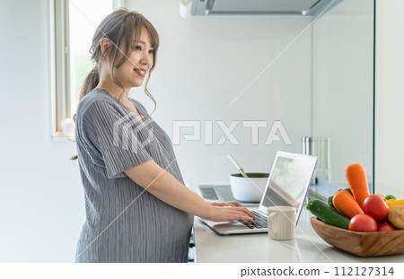 A pregnant woman keeps a food diary, records food, and manages meals on a computer in the kitchen. A pregnant woman keeps a food diary, records food, and manages meals on a computer in the kitchen. 112127314