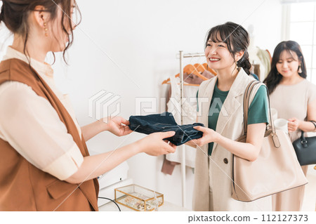 一位女顧客在服飾店購物後將牛仔褲交給收銀員。 112127373