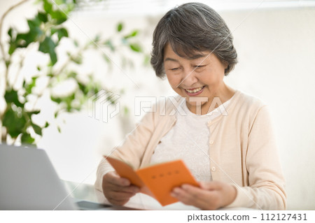 A senior woman using a computer while looking at her pension notebook, ending her life 112127431