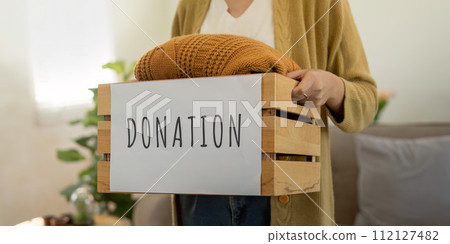 Donation, asian young woman sitting pack object at home, putting on stuff into donate box with second hand clothes, charity helping and needy people. Reuse recycle 112127482