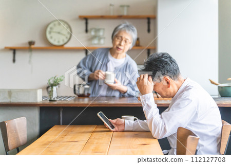 A senior man who has trouble using his smartphone at the dining table at home 112127708