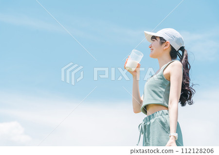 Young asian woman drinking protein while exercising under blue sky 112128206