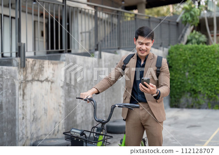 Asian businessman in a suit is riding a bicycle on the city streets for his morning commute to work. Eco transportation concept, sustainable lifestyle concept 112128707