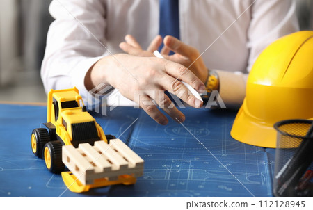 Man holds pencil, on table yellow helmet and truck 112128945