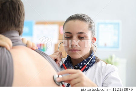 Woman therapist in clinic listens to lungs man 112128979