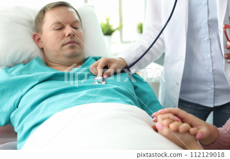 Sick man lies on bed in clinic, doctor examines 112129018