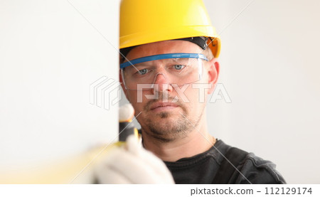 Repairman in helmet and mask, measures tape measure 112129174