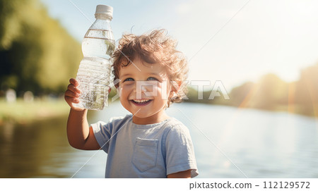 Poor, beggar, hungry smiling child eager to drink water from a plastic bottle. 112129572