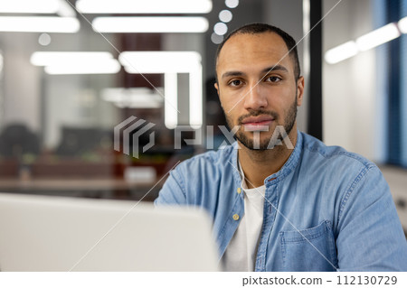 Focused professional man using a laptop in a well-lit contemporary office. The image conveys concepts of business, productivity, tech-savviness, and career-focused determination in a corporate Focused professional man using a laptop in a well-lit contemporary office. The image conveys concepts of business, productivity, tech-savviness, and career-focused determination in a corporate 112130729