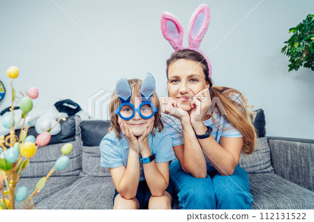 Portraits of happy smiling Caucasian mother and her son in bunny ears having fun at home on Easter day. Family sitting on sofa at home hugging, laughing. Family Easter traditions. Selective focus 112131522