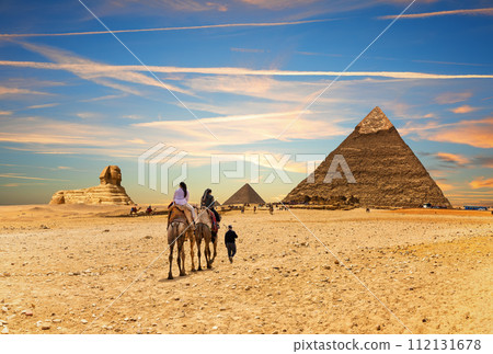 Tourists on camels with bedouin in front of the Great Pyramids of Egypt, Giza 112131678