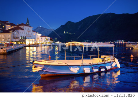 View of ancient picturesque city of Perast. Old medieval little town with red roofs and mountains on background of famous Kotor bay of Adriatic sea at blue hour. Travel in Montenegro. 112133820