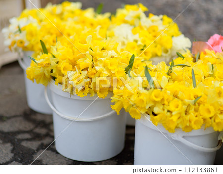 Selling of fresh daffodils at outdoor flower shop. Yellow and white Narcissus blossoms in a florist are sold at the street market 112133861