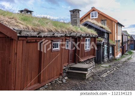 Gravel path in Roros, flanked by rustic wooden cabins with turf roofs Gravel path in Roros, flanked by rustic wooden cabins with turf roofs 112134123