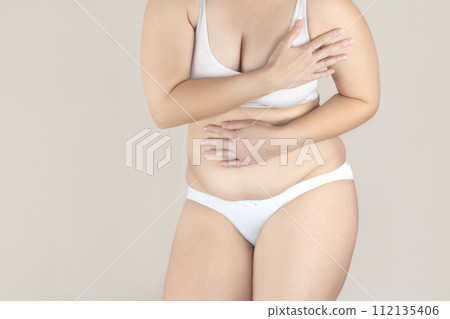 Plump woman with excess fat in white lingerie is embarrassed about her body, covering up Plump woman with excess fat in white lingerie is embarrassed about her body, covering up 112135406