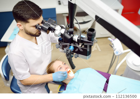 Dentist and patient at modern medical center. Doctor treats young woman teeth using microscope. Practitioner care the patient before orthodontists or prosthetics treatment. 112136500