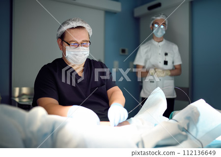 Professional vascular surgeon and assistant in the operating room of the clinic during vein surgery. Phlebectomy Professional vascular surgeon and assistant in the operating room of the clinic during vein surgery. Phlebectomy 112136649