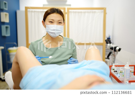 Gynecologist examines a patient laying on gynecological chair using medical vaginal speculum. Doctor takes a smear from a young woman cervix. Diagnosis of diseases. Gynecologist examines a patient laying on gynecological chair using medical vaginal speculum. Doctor takes a smear from a young woman cervix. Diagnosis of diseases. 112136681